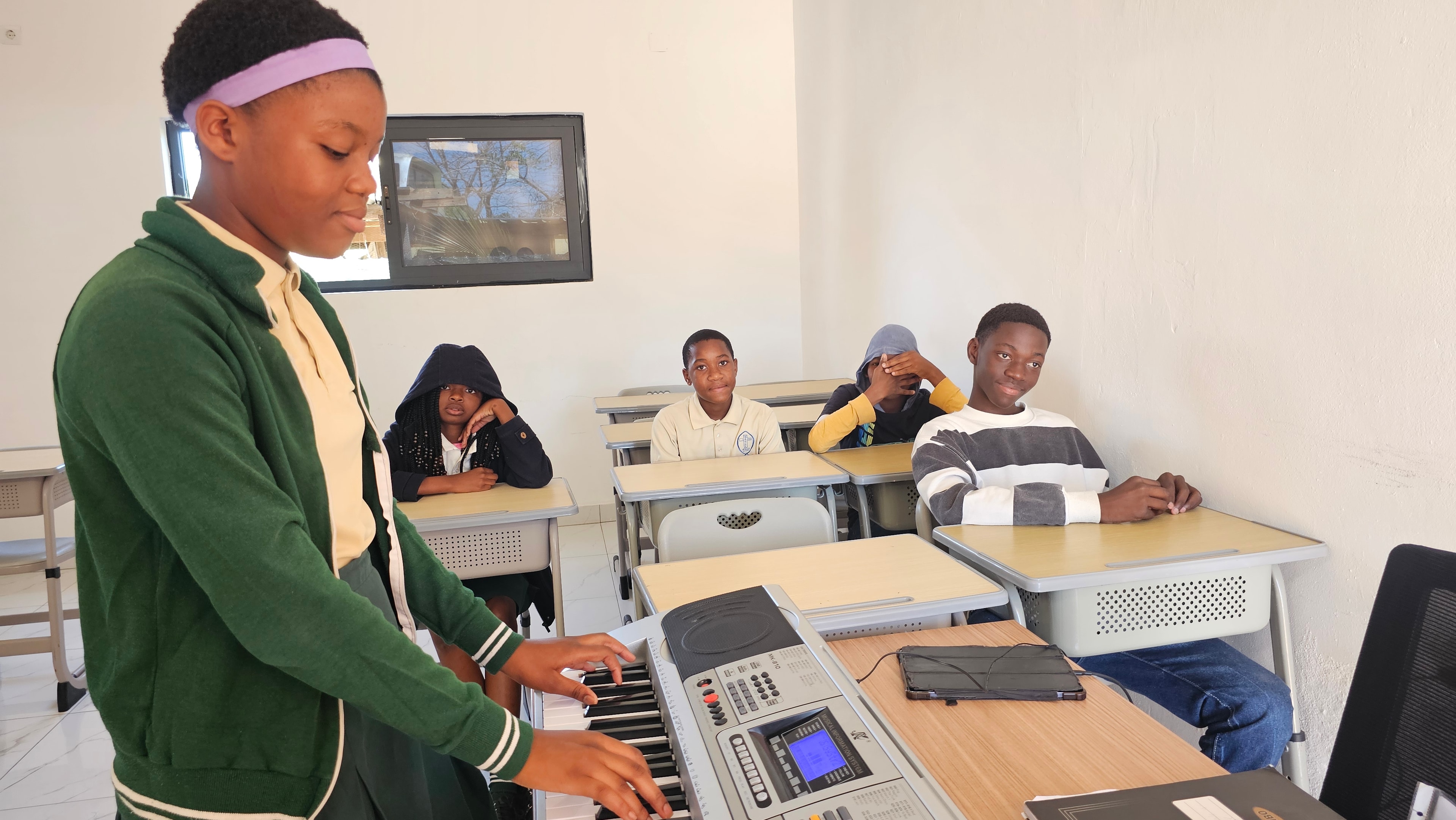 MGIS student performing on keyboard in music class while classmates watch