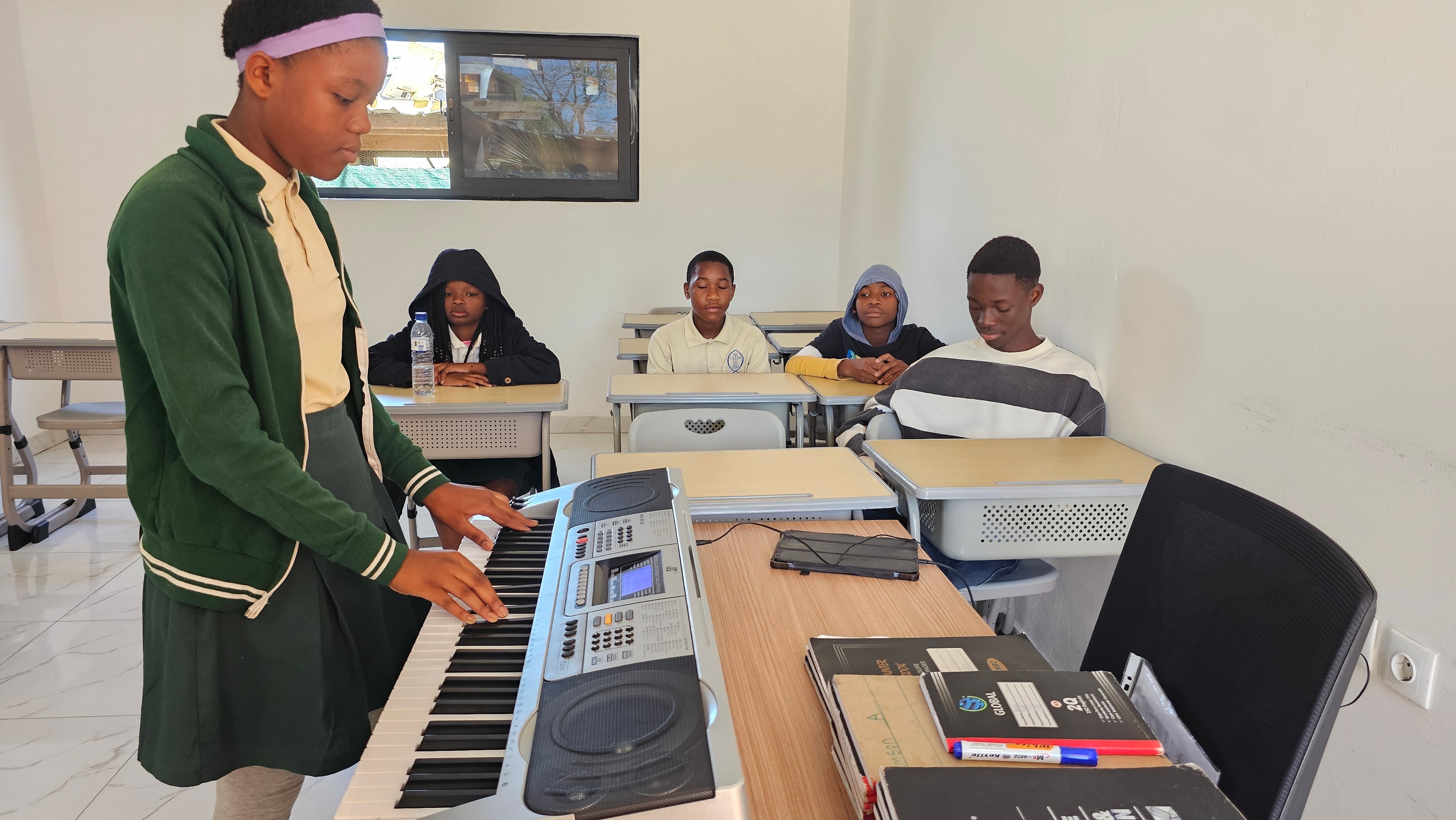 MGIS student playing keyboard during music lesson with attentive classmates